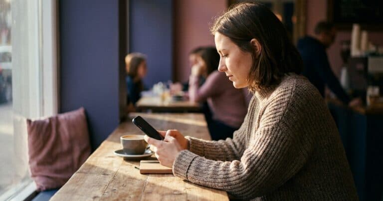 Frau scrollt am Cafétisch eine lange Liste auf dem Smartphone