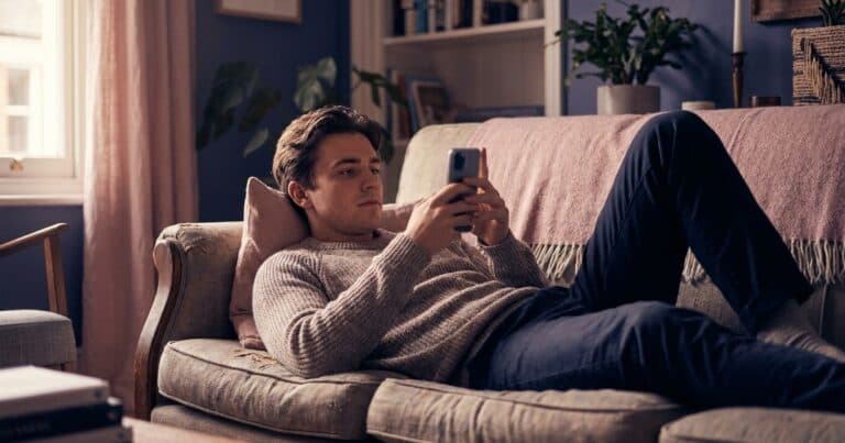 Junger Mann scrollt auf dem Sofa durch Instagram und überspringt Beiträge