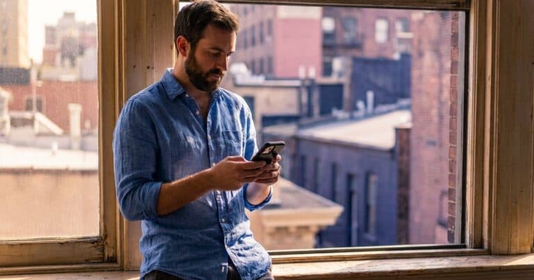 Mann am Fenster sieht auf dem Smartphone nach, wem jemand zuletzt gefolgt ist