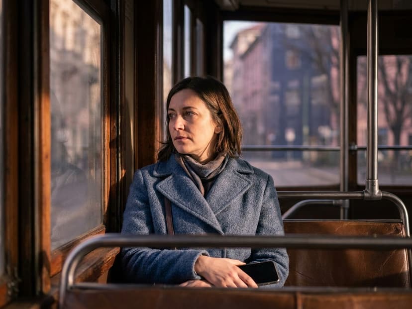 Frau schaut aus dem Straßenbahnfenster, das Smartphone im Schoß